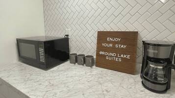 Una encimera de cocina con microondas, cuatro tazas, una cafetera y un cartel que dice "ENJOY YOUR STAY @ROUND LAKE SUITES".