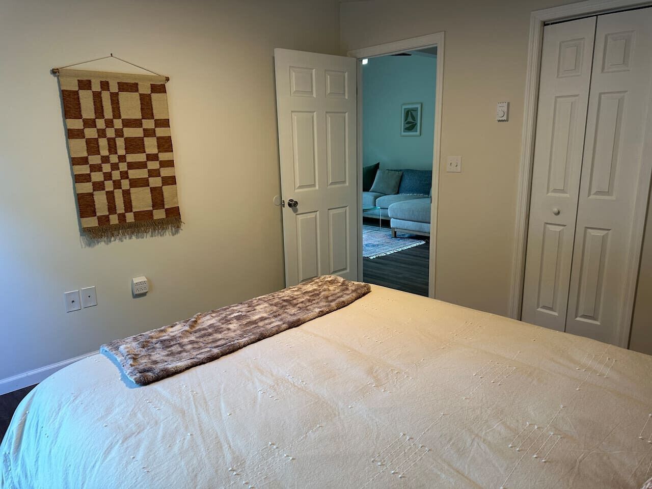A bedroom with a bed, a checkered blanket, and a door leading to another room.