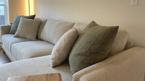 Un canapé beige agrémenté de plusieurs coussins, un lampadaire et une fenêtre avec des stores.