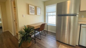 Una cocina compacta con un refrigerador de acero inoxidable, una mesa de madera con una silla y una planta en maceta.