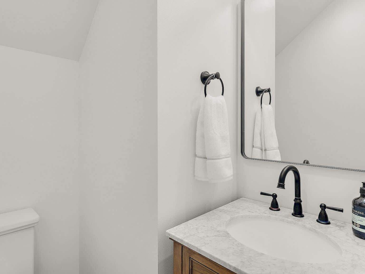 A modern bathroom with a white sink, black faucet, and a large mirror.