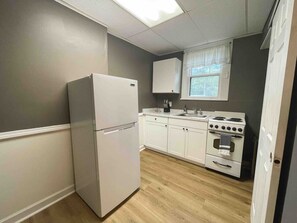 A compact kitchen with white appliances, a window with curtains, and a wooden floor.