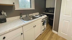 Une cuisine avec des meubles blancs, une cuisinière, un évier et une fenêtre avec des rideaux.