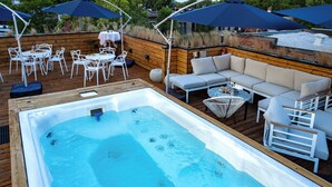 Un jacuzzi rodeado de mobiliario exterior, incluyendo un sofá y sillas, sobre una terraza de madera con sombrillas que dan sombra.