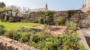 Un muro di pietra con un giardino antistante, una sedia in metallo e una piccola struttura in legno.