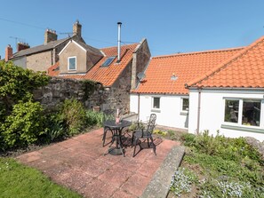 A patio with a table and chairs, surrounded by greenery and a stone wall. - Cygnet Cottage (Berwick-upon-Tweed)