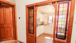 Una porta in legno con un vetro, che dà accesso a una cucina con mobili bianchi e un piano di lavoro in legno.