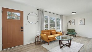 Una sala de estar con puerta de madera, un sofá, una mesa de centro de vidrio, una lámpara y una silla.
