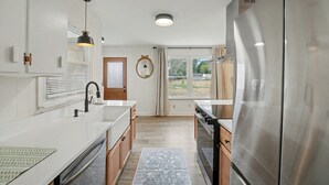 Cocina moderna con muebles blancos, electrodomésticos de acero inoxidable y un amplio ventanal con vistas al exterior.