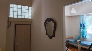 A room with a wooden door, a mirror, a window with frosted glass, a bed with a blue and white patterned bedspread, and a standing fan. - Yr Olewydden, a 2-bedroom house in a tranquil neighborhood of authentic Piraeus (Keratsini)