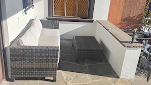 A patio area with wicker furniture, a stone floor, and a window with a decorative grille. - Quiet vacation apartment with terrace and garden - wellness use included. (Reutte)