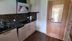 A kitchen with a black countertop, white cabinets, a coffee machine, and a wooden door. - Quiet vacation apartment with terrace and garden - wellness use included. (Reutte)