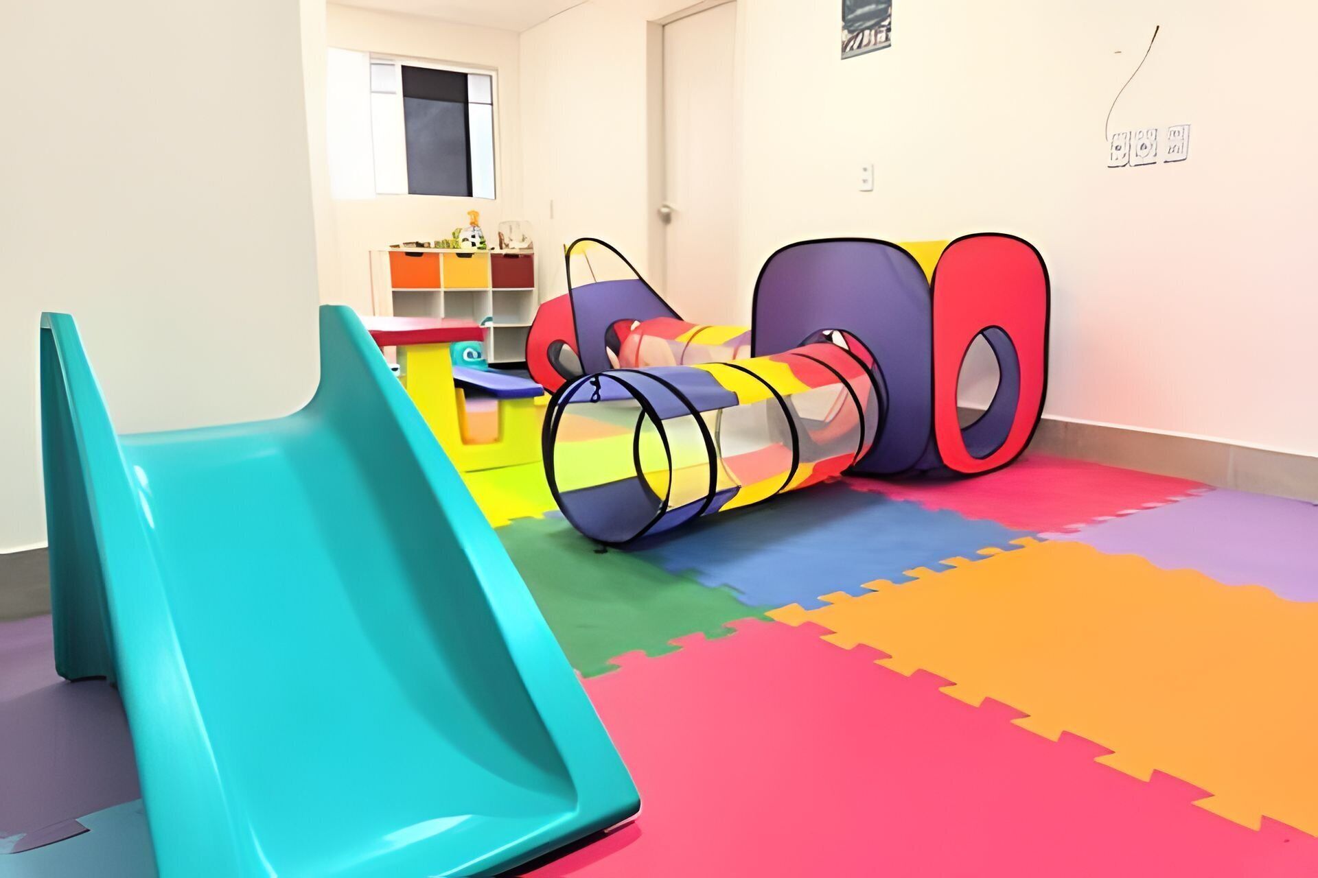Un espace de jeux avec un toboggan, des tapis de jeu en mousse de couleurs vives et une voiture jouet.