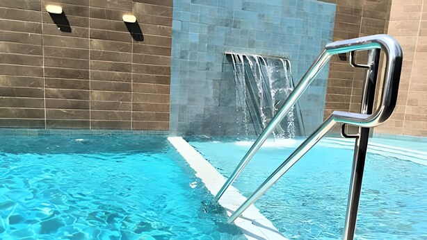 A swimming pool with clear blue water, a metal pool ladder, and a waterfall feature. - Aline Duque by Temporada Inn (Ipojuca)