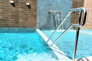 Una piscina con acqua cristallina azzurra, una scala in metallo e una cascata.