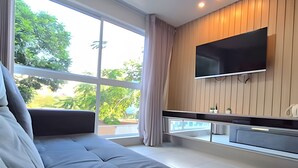 A modern living room with a large window, a flat-screen TV mounted on the wall, and a sofa. - Aline Duque by Temporada Inn (Ipojuca)