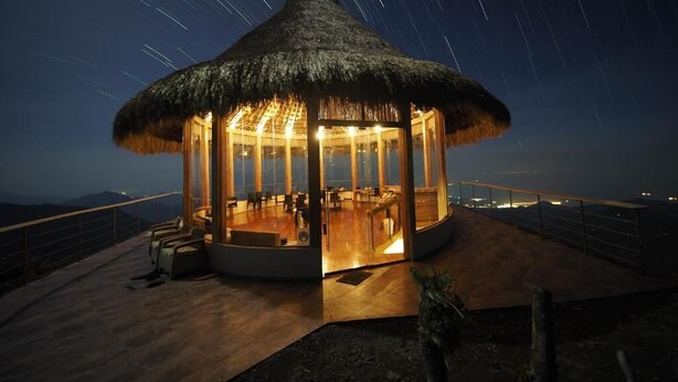 A thatched-roof structure with a glass enclosure, a wooden deck, and a view of the night sky. - Minca El Dorado Reserve (Minca)