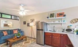 Un espacio habitable compacto con kitchenette, un sofá, una mesita de centro y un ventilador de techo.