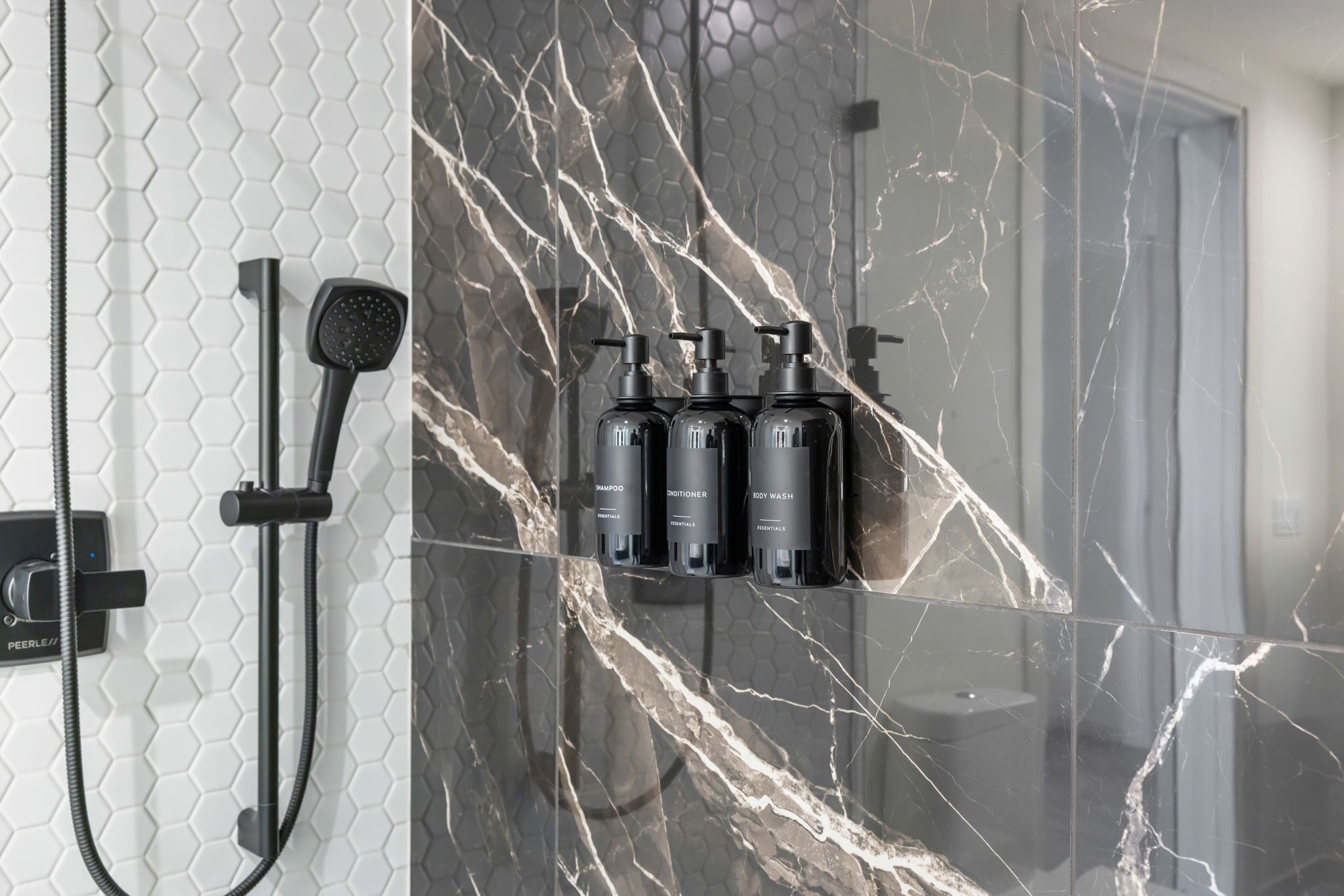 Ein Badezimmer mit Dusche, einem gläsernen Regal mit drei Flaschen und einer Wand mit sechseckigem Muster.