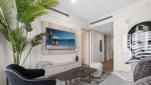 Un salon moderne avec une grande plante, un tableau représentant une plage, une table à manger et un canapé.