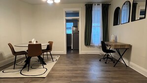 Un coin repas avec une table ronde et des chaises, un petit bureau en bois avec une chaise, et un réfrigérateur à l’arrière-plan.