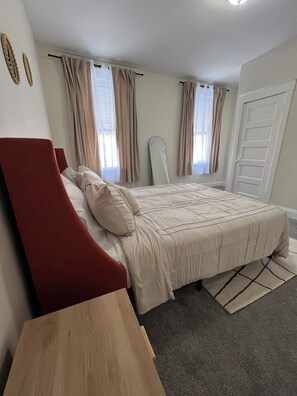 Une chambre à coucher avec un lit, une chaise rouge, une table en bois et un miroir.