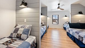 Una habitación con dos camas, ventilador de techo, una ventana y una lámpara fijada a la pared.