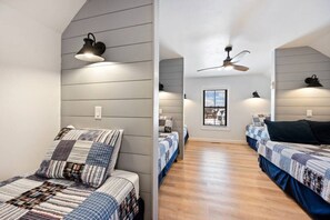 Ein Zimmer mit zwei Betten, einem Deckenventilator, einem Fenster und einer Wandlampe.
