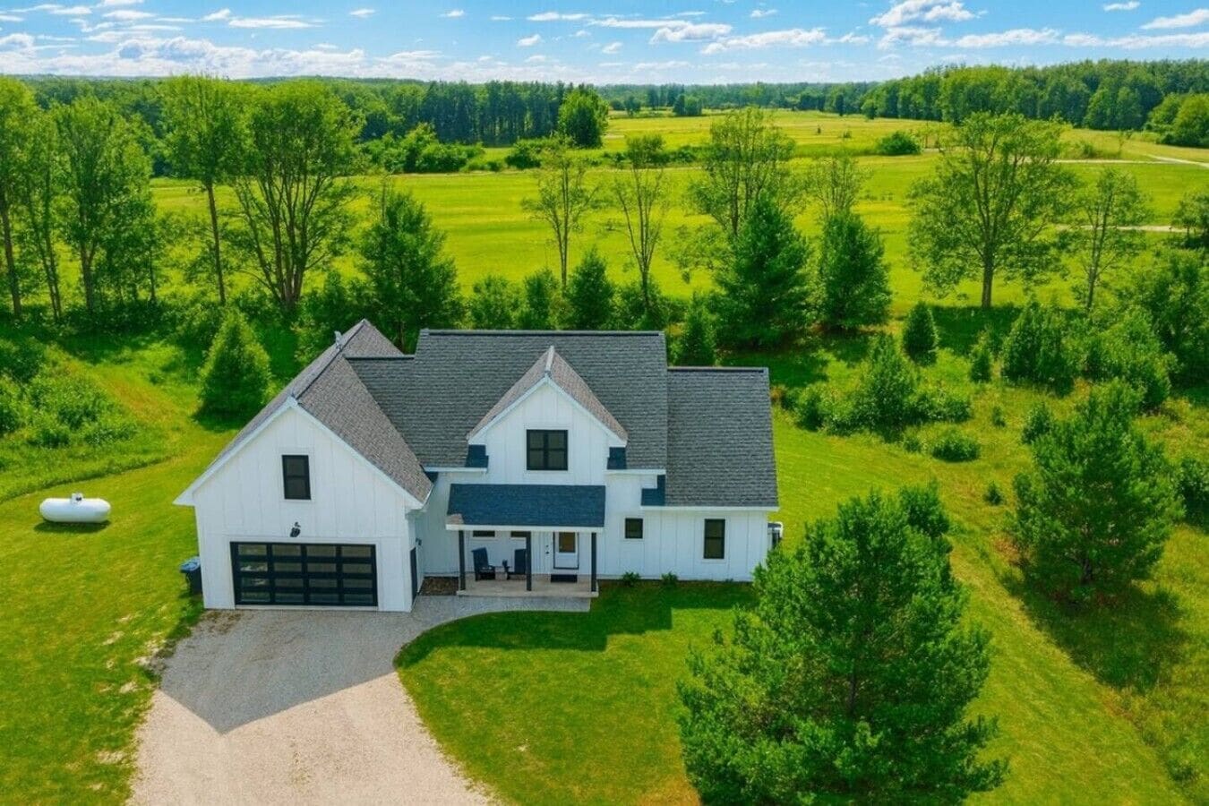A two-story house with a garage, surrounded by lush green fields and trees.