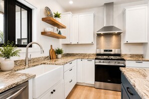 Una cocina moderna con armarios blancos, estufa de acero inoxidable y encimera de granito.