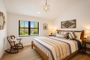 Een slaapkamer met een groot bed, een schommelstoel, een raam met jaloezieën, een ster-vormige lamp en een wanddecoratie met een chevron-patroon.