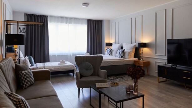 Ett modernt hotellrum med en soffa, en fåtölj och en säng med en TV och lampor.