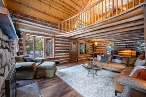 Ein Blockhaus-Interieur mit einer Steinwand, einer Holztreppe, einem Sofa, einem Couchtisch und großen Fenstern.