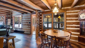 Interno di una baita di legno con zona pranzo, pavimento in legno e una grande finestra.