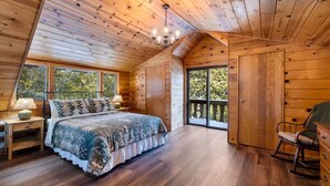 Camera da letto in una baita di legno, con un letto, un comodino, una cassettiera e un'ampia finestra.