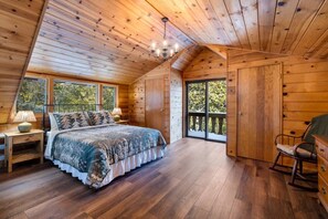 Ein Schlafzimmer einer Holzhütte mit einem Bett, einem Nachttisch, einer Kommode und einem großen Fenster.