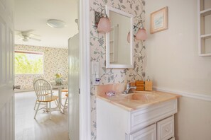 A bathroom with a floral wallpaper, a white vanity, a mirror, and a ceiling fan. - Serene 1-bedroom cottage with AC in charming Thonotosassa (Thonotosassa)