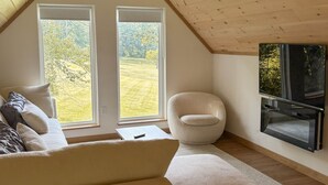 A loft-style room with a sloped ceiling, a sofa, a chair, a fireplace, and a large window.