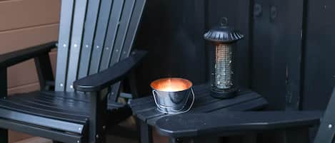 Dos sillas Adirondack negras, una mesita y un farol en una terraza de madera.