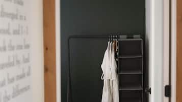 Una habitación con piso de madera, pared oscura y armario metálico negro con ropa colgada.