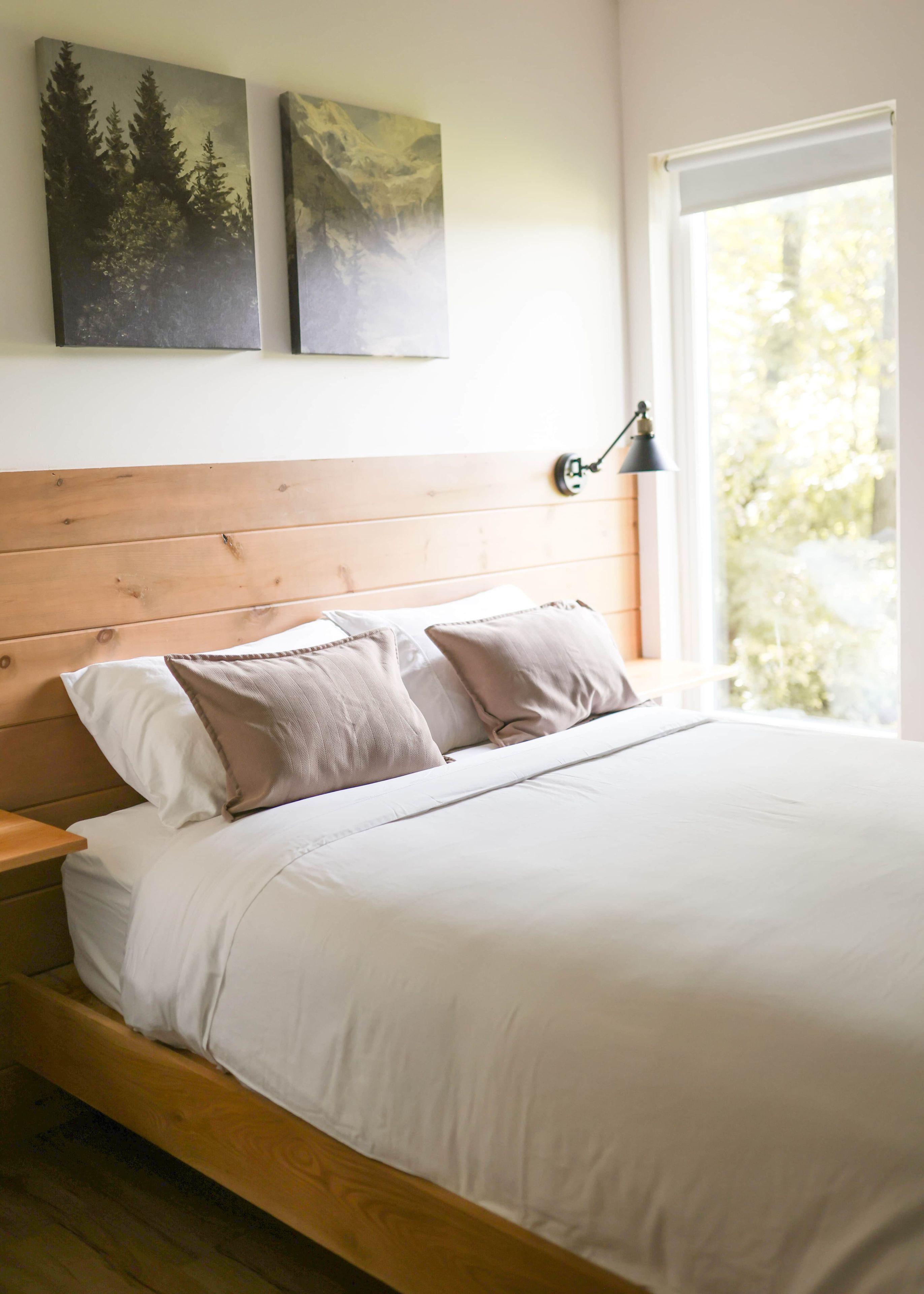 Ein Schlafzimmer mit einem Holz-Kopfteil, einem Bett mit weißer Bettwäsche, zwei Kissen, einer Nachttischlampe und einem Bild an der Wand.