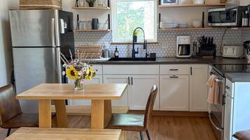 A modern kitchen with a wooden table, chairs, a refrigerator, microwave, and a sink.