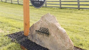 A sign for White Oak Stays with a wooden post and a large rock with the address 4888 Yackey Dr.