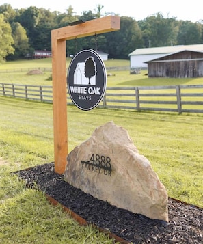 Señal para White Oak Stays, con un poste de madera y una gran roca con el número 4888 Yackey Dr.