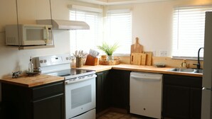 Una cocina con microondas, estufa, lavavajillas, encimera de madera y una ventana con persianas.