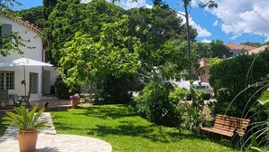 Ein gepflegter Garten mit einem Kiesweg, der zu einem weißen Gebäude mit grünen Fensterläden führt.