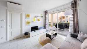 Una sala de estar moderna con un sofá, una mesa de centro, un televisor y un ventanal corredizo que da a un espacio exterior.