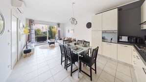 Una cocina moderna con armarios blancos, un comedor con mesa de vidrio y vistas al exterior.