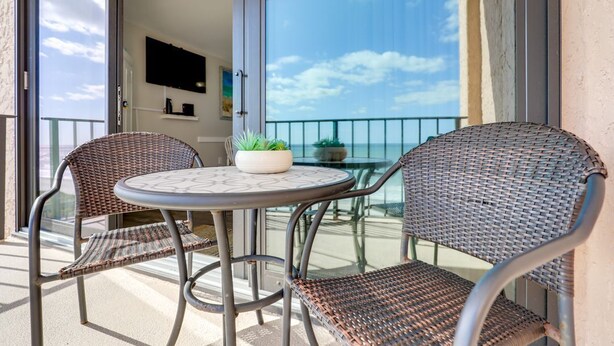 A balcony with wicker chairs, a round table, and a potted plant. - Wake Up to Waves | Stunning Oceanfront Condo (North Myrtle Beach)