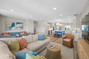 A modern living room with a sofa, wicker chair, and a dining area with a table and chairs.
